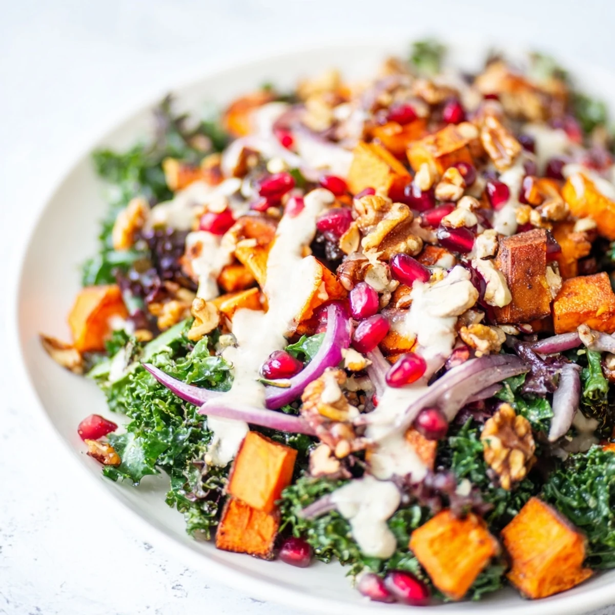 Golden roasted root vegetables rest on mixed winter greens, pomegranate seeds, and walnuts, drizzled with creamy tahini dressing for the Snowy Day Vegan Salad.