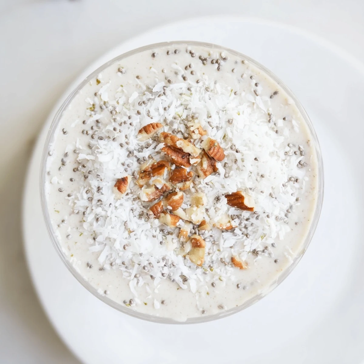 A vibrant Snowy Day Paleo Smoothie in a frosted glass, garnished with shredded coconut and nuts on a rustic wooden table.
