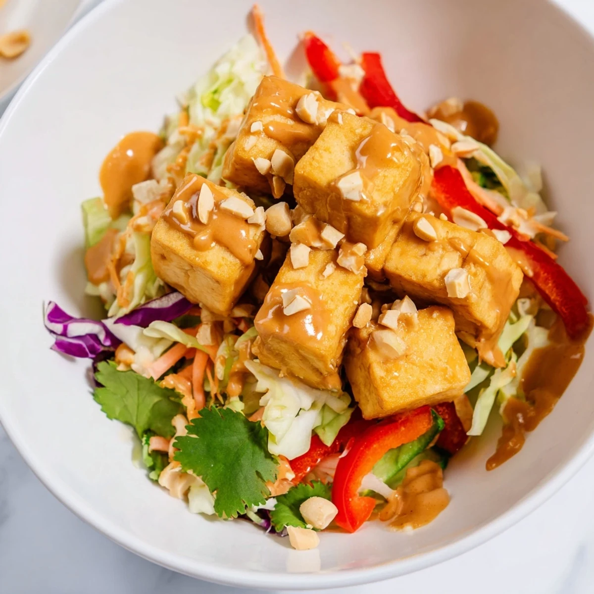 A close-up of the Spicy Peanut Tofu and Cabbage Crunch Bowl garnished with lime wedges and peanuts. 