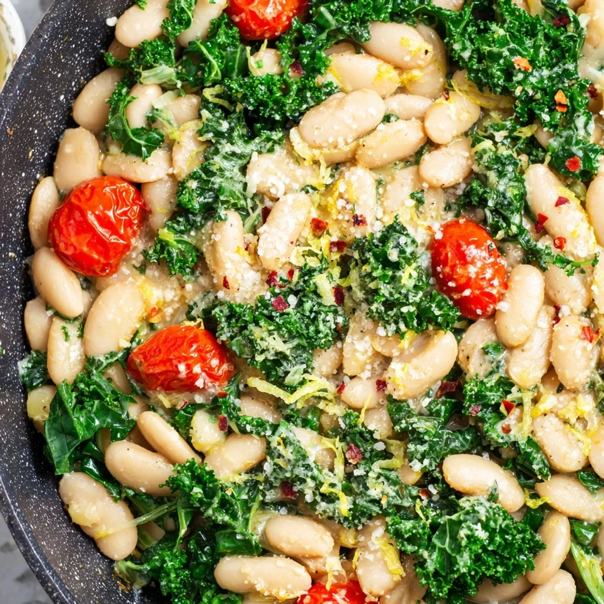 A close-up of the Herby White Bean and Kale Skillet showing vibrant green kale leaves and creamy white beans in a rustic ceramic pan.