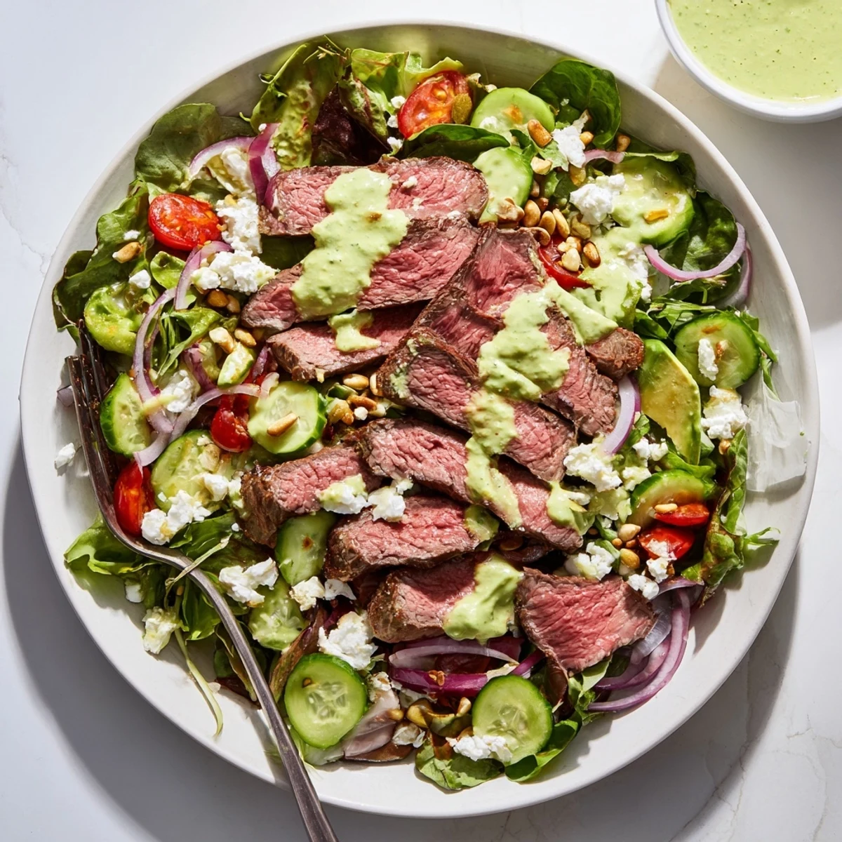 Juicy, medium-rare steak slices rest atop a bed of crisp mixed greens and veggies in the Garlic Herb Steak Salad With Avocado Lime Dressing.