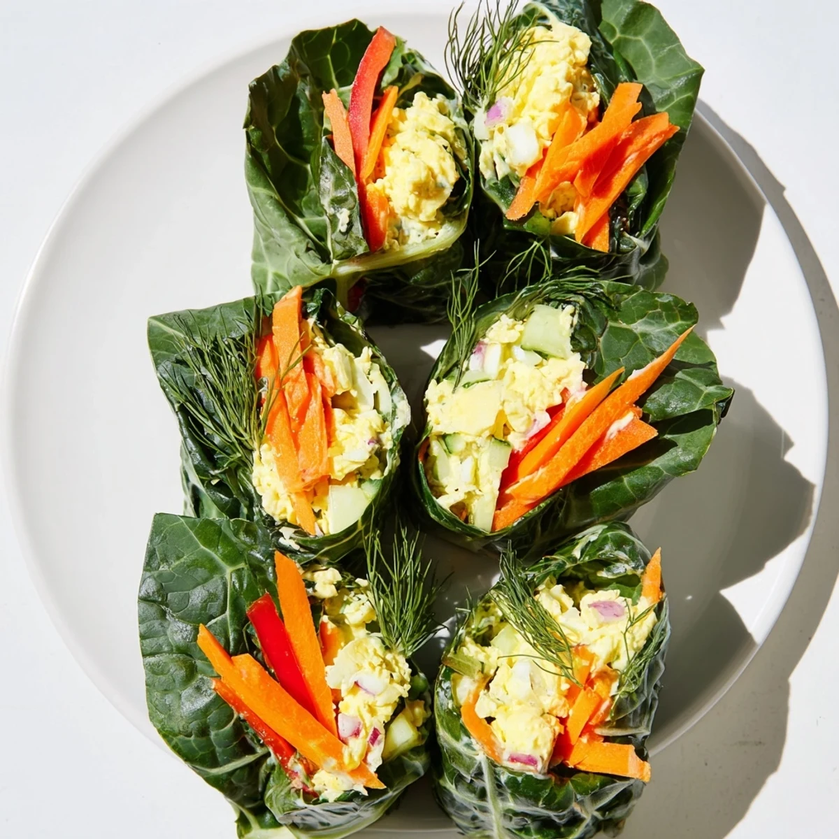 Perfectly rolled Avocado Egg Salad Collard Wraps showcasing the vibrant egg salad and crisp carrot, cucumber, and bell pepper toppings.