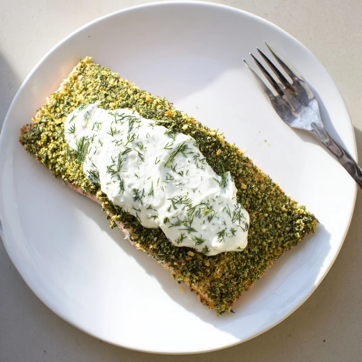 Close up of Herb Crusted Salmon With Creamy Dill Sauce highlighting the flaky fish and creamy green herb garnish.