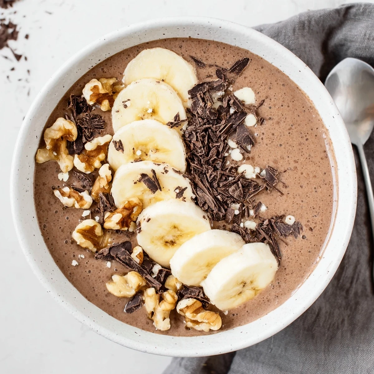 Creamy chocolate banana protein chia cream topped with fresh banana slices and dark chocolate shavings in a glass bowl