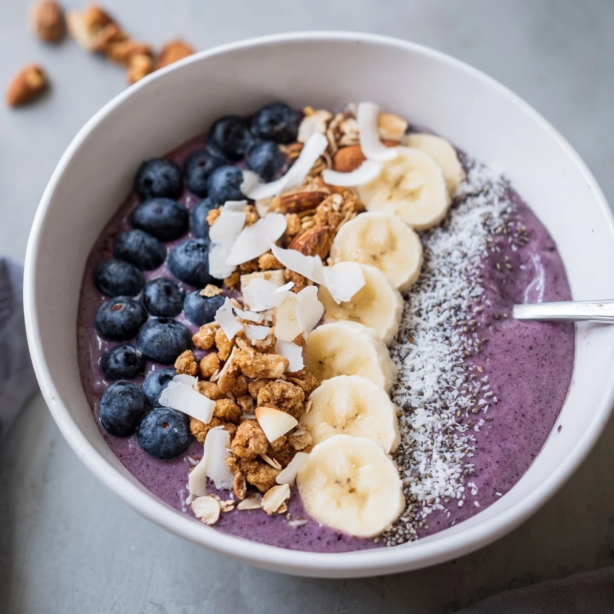 Thick purple smoothie bowl layered with blueberries, chia seeds and crunchy almond slices