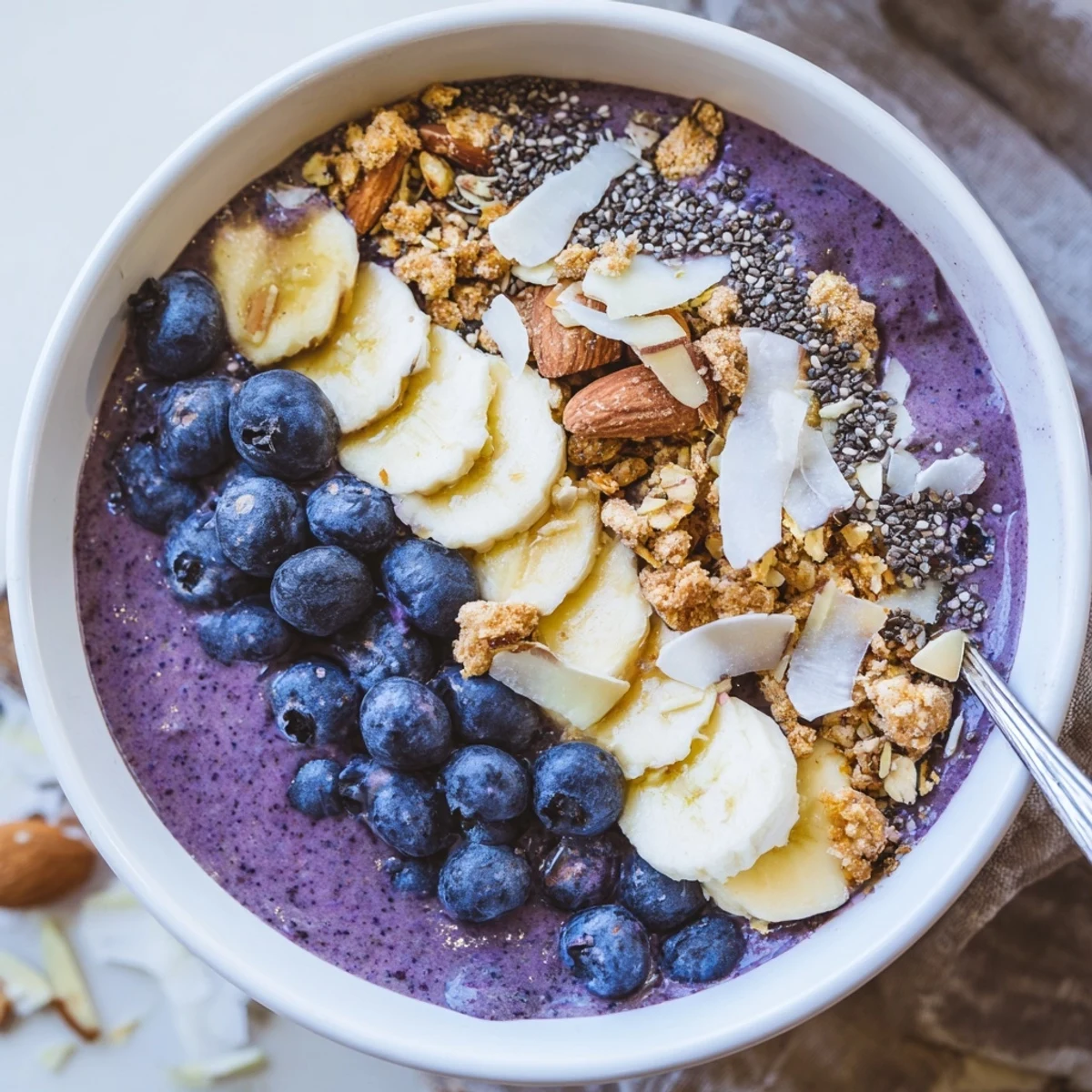 Vibrant blueberry coconut protein smoothie bowl topped with fresh fruit, granola and shredded coconut