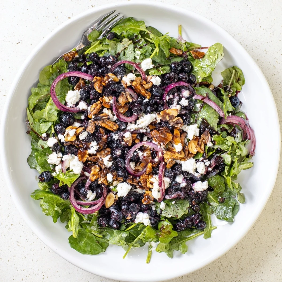 Colorful bowl of roasted blueberry and arugula salad drizzled with balsamic vinaigrette and almond clusters