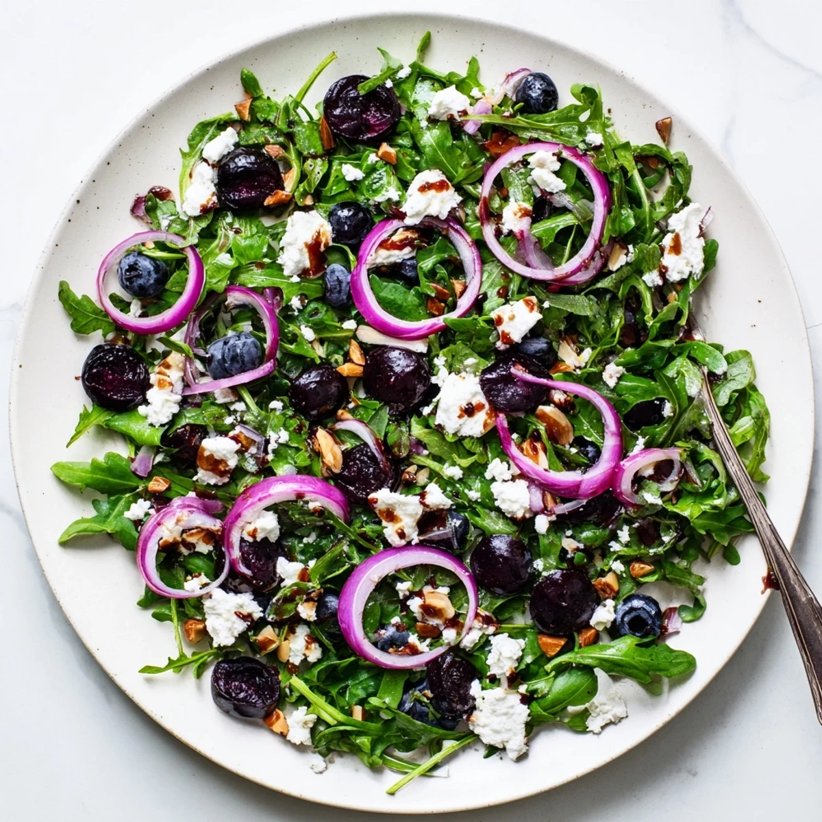 Vibrant roasted blueberry and arugula salad plated with crumbled goat cheese and golden almond crunch topping