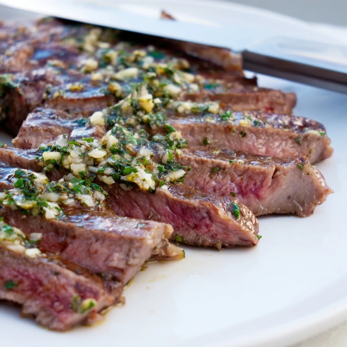 Sliced garlic herb steak arranged on a white platter with colorful roasted spring vegetables including carrots, asparagus, radishes, and snap peas, garnished with fresh chives.