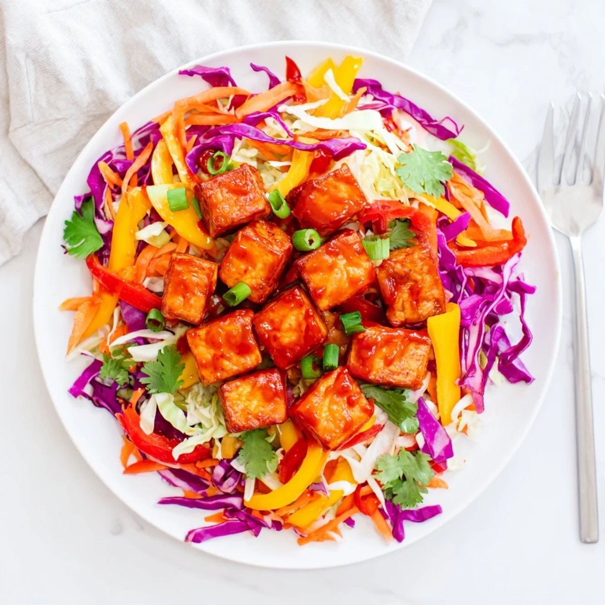 Golden crispy Sriracha tofu cubes plated over vibrant rainbow vegetable slaw