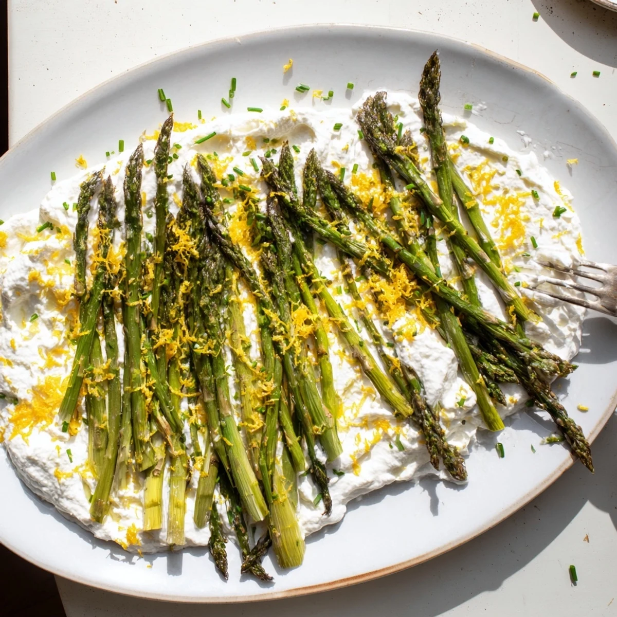 Tender roasted asparagus spears arranged atop a creamy whipped lemon ricotta on a white serving platter