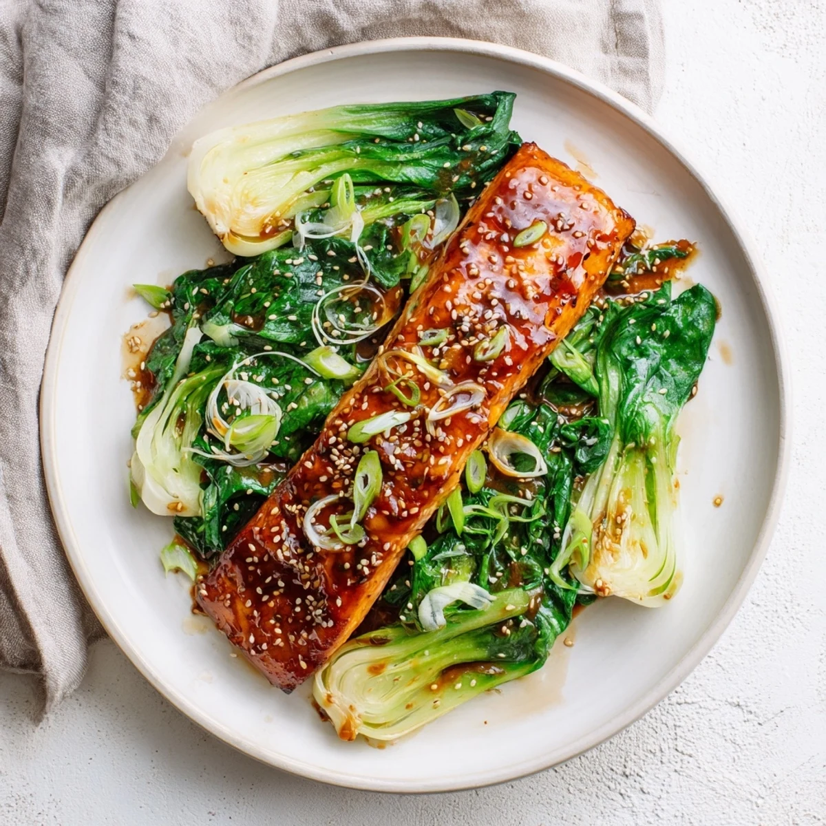 Golden glazed miso maple salmon fillets resting atop vibrant sesame dressed greens with spring onion garnish