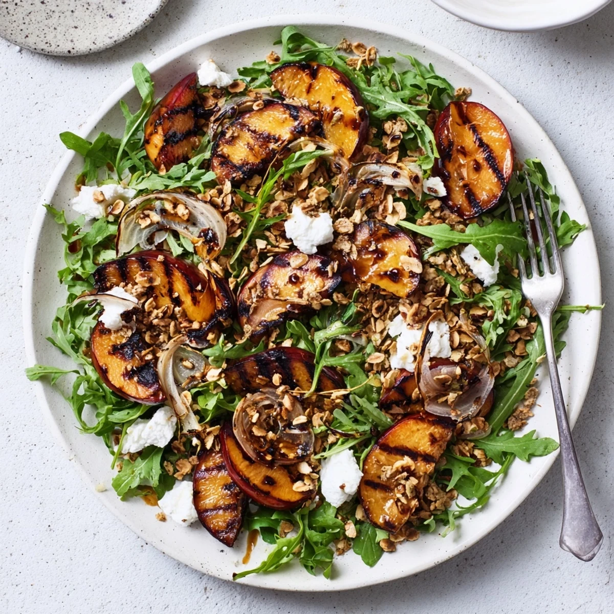 Colorful grilled plum and arugula salad topped with creamy goat cheese and crunchy almond crumble