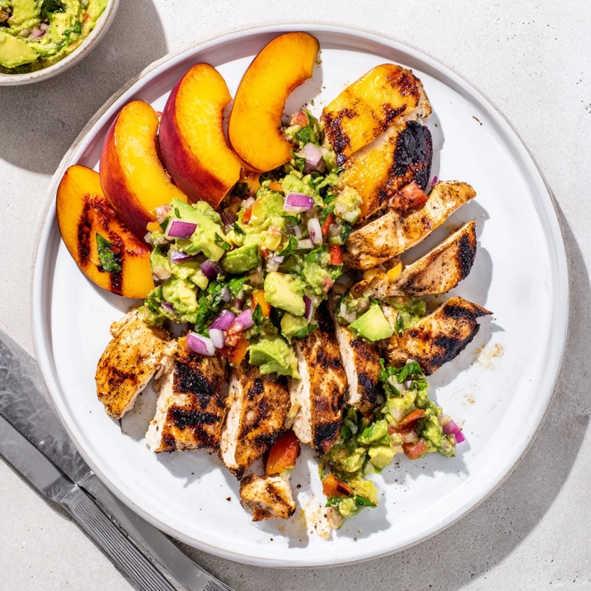 Summer dinner featuring juicy grilled chicken with grilled peach halves and chunky basil avocado salsa