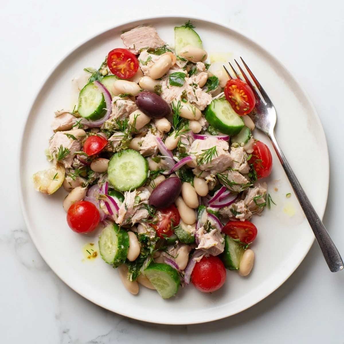 Fresh Mediterranean tuna white bean salad plated with crisp red onion, Kalamata olives, and lemon herb dressing