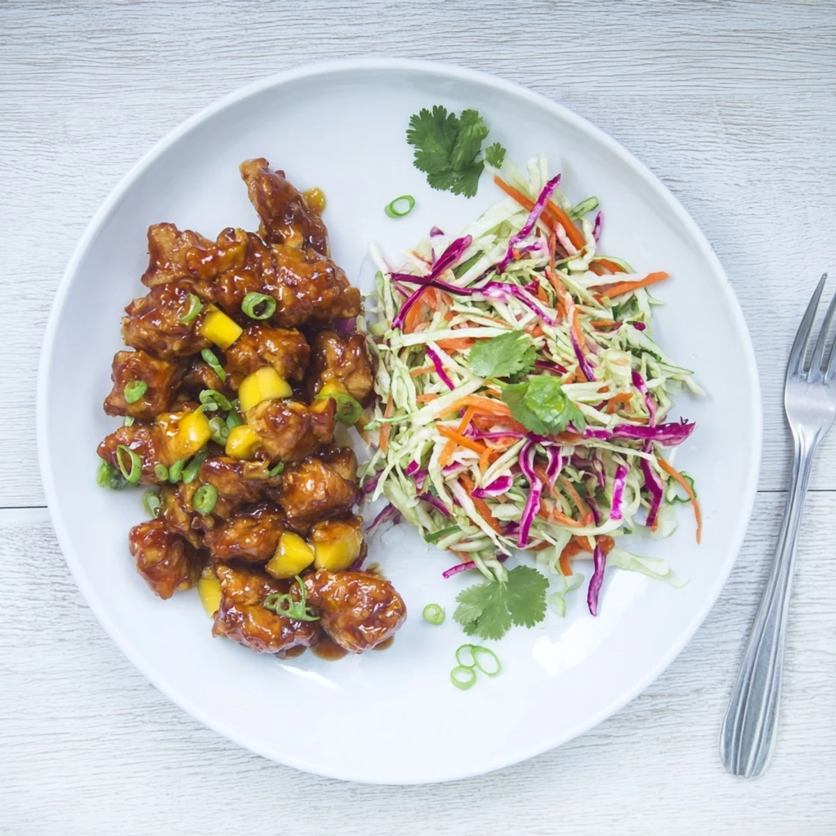 Juicy spicy mango chicken plated with tangy cabbage slaw garnished with carrots and green onions