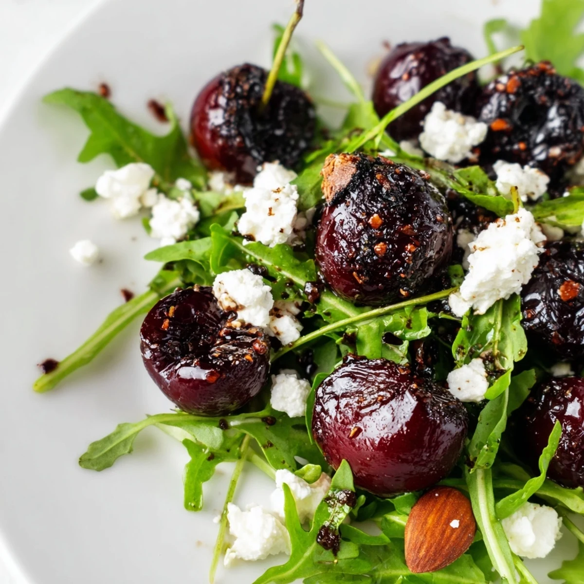 Vibrant bowl of grilled cherry arugula salad topped with crumbled goat cheese and golden almonds