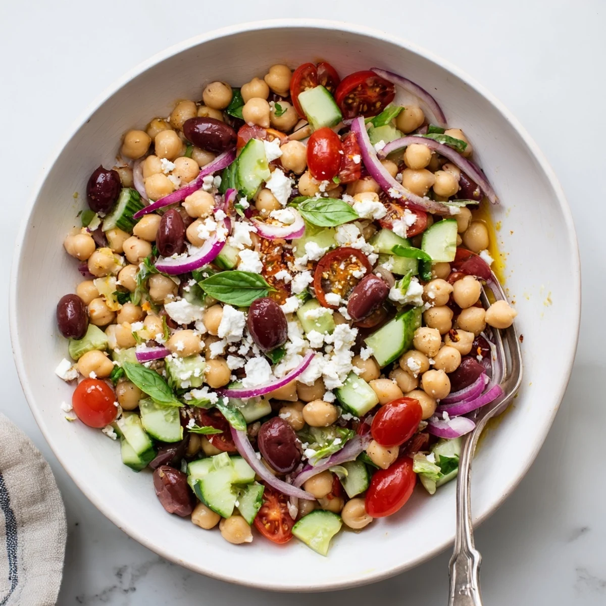 Vibrant bowl of chickpea tomato basil salad featuring red cherry tomatoes, cucumber, olives, and green basil