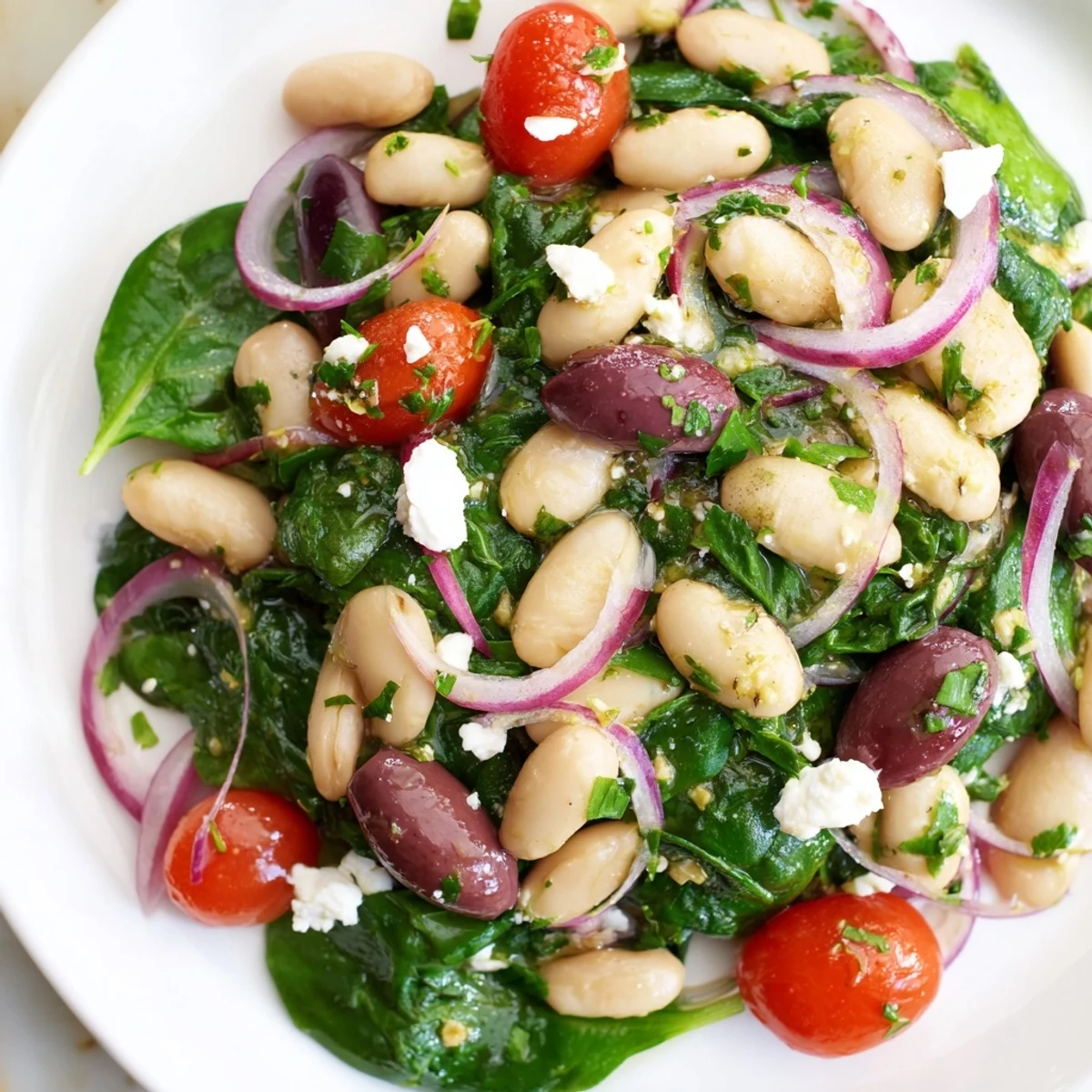 Creamy white beans and fresh spinach star in this Mediterranean olive salad tossed with juicy tomatoes and bright lemon herb dressing on a rustic serving platter