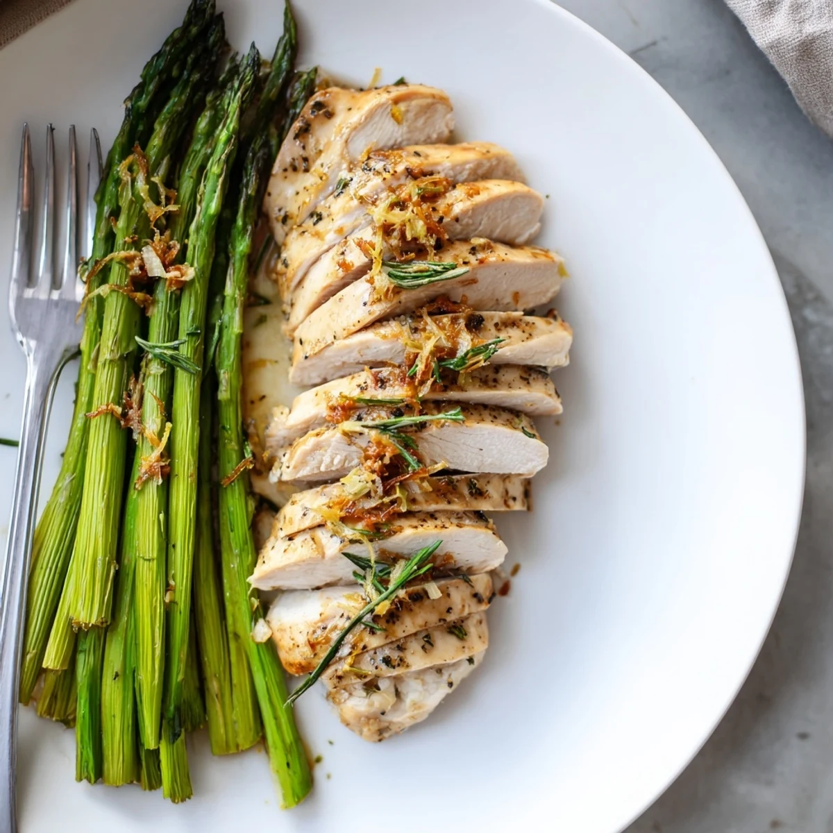 Crispy garlic herb chicken with roasted asparagus garnished with fresh lemon and rosemary